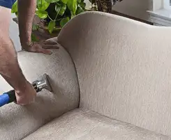 Professional upholstery cleaner deep-cleaning a fabric sofa with a handheld extraction tool and hose in New Haven, CT.